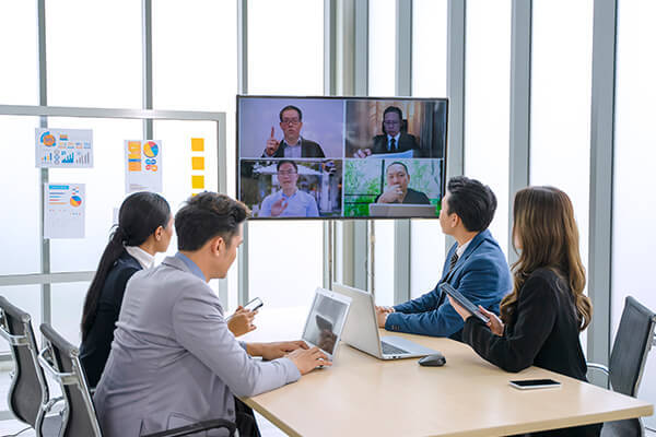 A group of workers in a conference room engaging in a video call