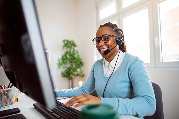 Business U Caa S Sub Hero 600x400 Woman at desk with headset on talking on phone while working at computer