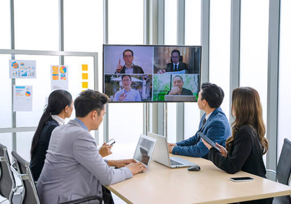 A group of workers in a conference room engaging in a video call