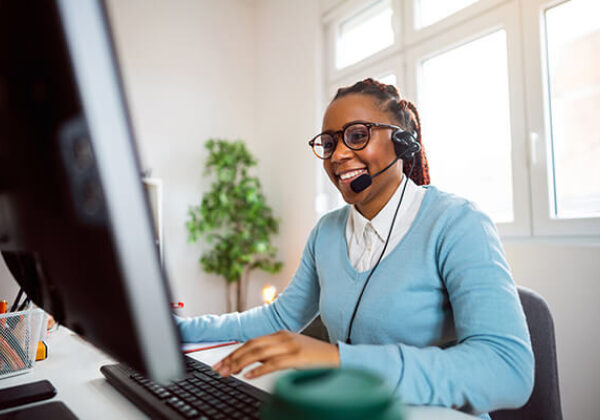 Business U Caa S Sub Hero 600x400 Woman at desk with headset on talking on phone while working at computer