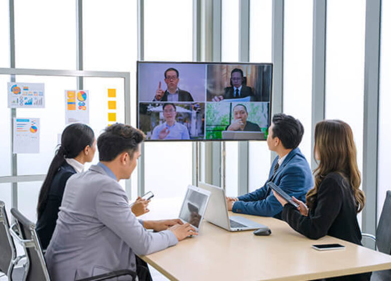 A group of workers in a conference room engaging in a video call